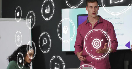 Presenting man wearing shirt gesturing at digital display in office, with laptop, icons, copy space....