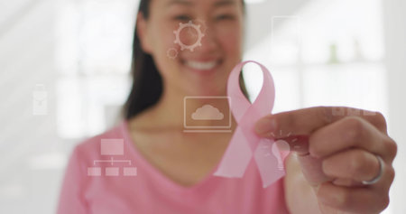 Holding pink awareness ribbon in office, Korean woman wearing pink shirt with silver ring and icons. Advocacy, empowerment, technology, healthcare, femininity, professionalism, inspirationの写真素材