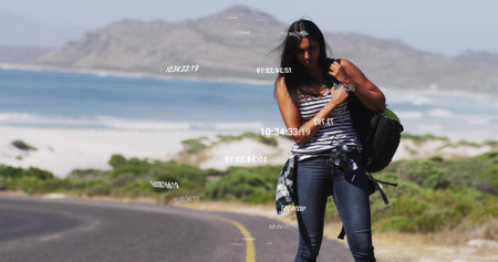 Adjusting woman securing backpack strap on coastal road with plaid shirt around waist, copy space....