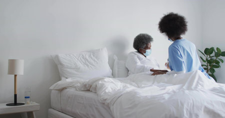 Leaning healthcare worker in scrubs holding gowned patient arm at bedside with lamp, copy space. Medical staff, patient care, compassion, hospital environment, wellness, healthcare, supportの写真素材
