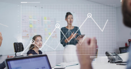 Presenting businesswoman pointing at digital graph overlay in conference room, with tablet....