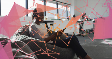 Mid adult woman wearing headset holding tablet sitting on beanbag in office lounge, with terrarium....