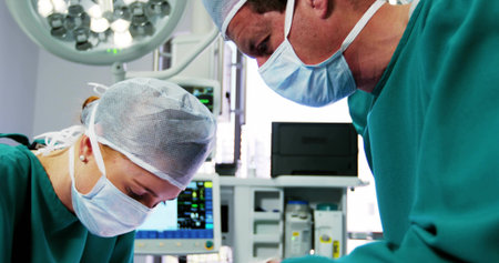 Operating surgeon and assistant performing surgery in OR, with scrubs, masks, light and monitor. Medical, healthcare, surgical, clinical, sterile, professional, hospitalの写真素材