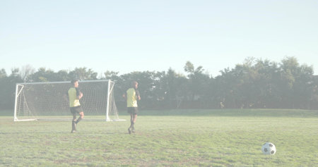 Jogging players wearing training vests, black shorts on park field, with portable goal, soccer ball. Athletic, teamwork, exercise, outdoor, vibrant, motivation, fitnessの写真素材