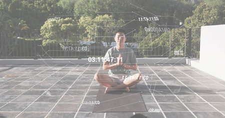 Meditating Asian male sitting on yoga mat on terrace with railing and holographic data overlays....