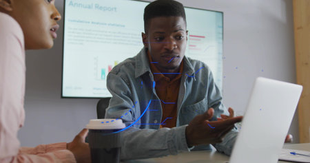 Colleagues reviewing annual report in office meeting room, with screen, laptop takeaway coffee cup....