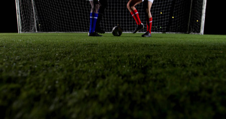 Contesting ball between two male players on nighttime soccer field, with turf, goal net, cleats. Sports, competition, fitness, athleticism, teamwork, outdoor, vitalityの写真素材