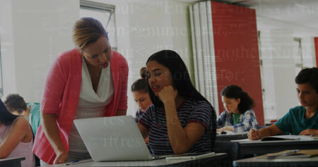 Leaning educator guiding student on laptop in modern classroom, with notebooks and textbooks. Learning, mentorship, collaboration, education, academic, digital, professionalの写真素材