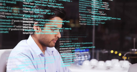 Typing code Asian man wearing blue shirt at office desk, with glass code reflections and cups....