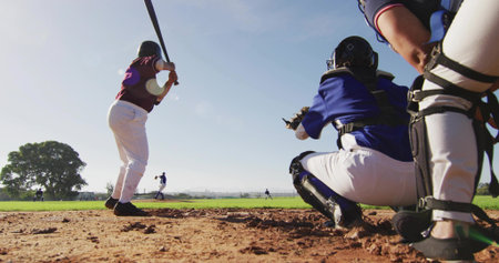 Batting, maroon batter swinging in batter's box at baseball field, catcher in blue gear, copy space. Diamond, youth, female, sport, outdoors, action, pitcherの写真素材