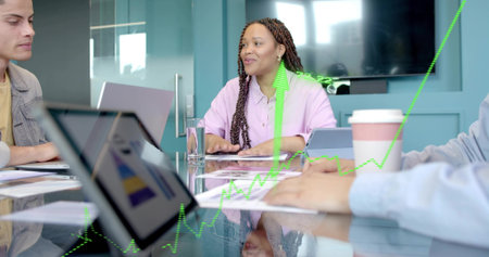 Leading woman in lavender blouse guiding meeting at conference table with laptops and graph overlay. Collaboration, teamwork, business, enterprise, corporate, modern, professionalの写真素材