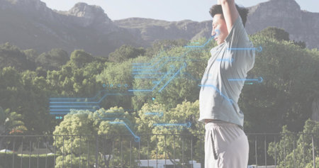 Stretching Asian man raising arms on terrace, with railing and blue overlay graphics, copy space....