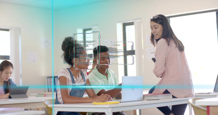 Leaning teacher wearing pink blazer guiding two students using laptop in classroom with tablet....