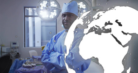 Standing scrub-clad surgeon crossing arms in hospital OR, with tray and globe overlay, copy space. Medical, healthcare, professional, sterile, clinical, innovation, precisionの写真素材