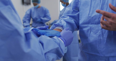 Donning gloves surgical team preparing for surgery in operating room with gowns and surgical lights....