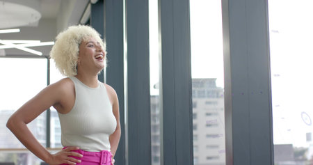 Laughing woman wearing white top and pink pants near glass wall with chart markings, copy space....