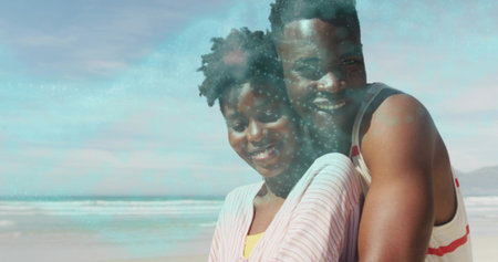 Hugging adult couple wearing pink striped shirt and white tank top on sandy ocean edge. Romance, serenity, outdoor, leisure, happiness, intimacy, naturalの写真素材