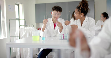 Using dropper and test tube, lab partners wearing labcoats goggles at school lab with neon beakers. Science, education, innovation, experimentation, collaboration, learning, environmentの写真素材