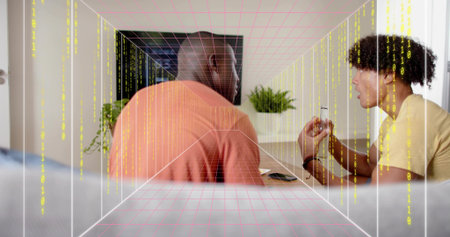 Sitting men in orange, yellow shirts demonstrating small device at home with smartphone, pink grid. Collaboration, gadget, tech, livingroom, plant, television, discussionの写真素材