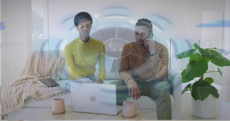 Sitting coworkers collaborating on laptop at coffee table in living room with mugs blanket plant. Collaboration, workspace, modern, comfortable, interior, productivity, friendshipの写真素材