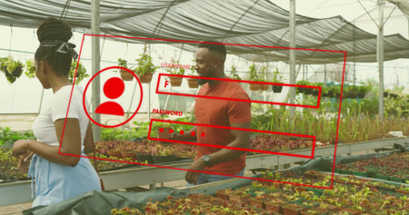 Gesturing horticulturists in red polo and apron examining seedling trays on benches in greenhouse....