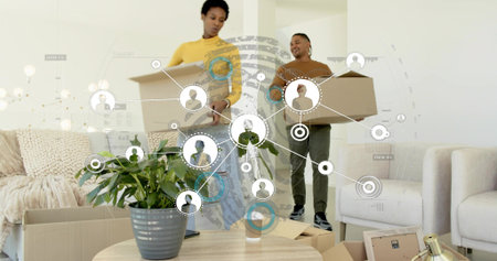 Couple carrying moving boxes inside living room, coffee table with plant and cup, network overlay....