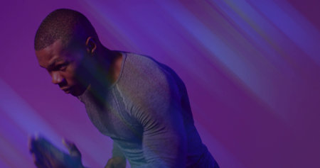 Leaning man in gray sportswear raising arms at chest in studio, with blue green light streaks....