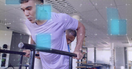 Pushing man in lavender tee and dark shorts on parallel dip bars at gym, spotter assisting. Fitness, training, duo, strength, kettlebell, motion, sunlitの写真素材