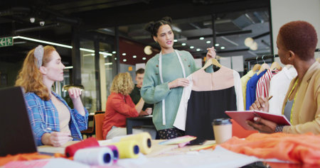 Holding wooden hanger, fashion designer showcasing two-tone dress in studio with swatches. Creativity, teamwork, innovation, craftsmanship, inspiration, artistry, professionalの写真素材