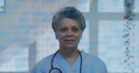 Standing senior medical professional in blue scrubs in clinic with stethoscope and binary overlay. Healthcare, digital, innovation, professionalism, diagnosis, mentorship, botanicalの写真素材