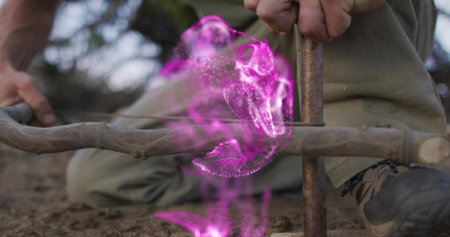 Creating man kneeling generating flame using spindle drill on forest soil, with energy swirl....