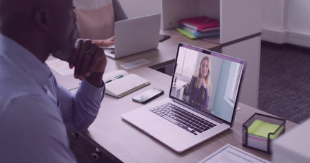 Displaying smiling collaborator on office laptop at desk, with smartphone notebook and paper tray. Collaboration, teamwork, professional, modern, workspace, communication, productivityの写真素材