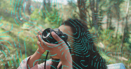 Adult woman in pink jacket framing shot in woods, with DSLR camera strap and turquoise lines....