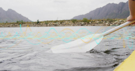 Dipping white paddle blade into rippling water on lake shoreline, yellow kayak rim, copy space....
