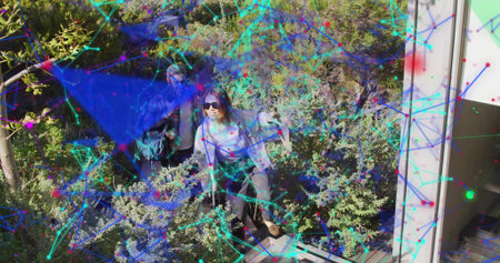 Mature man and woman examining digital network overlay amid shrubs on metal walkway, backpacks. Technology, cybersecurity, connectivity, outdoor adventure, surveillance, urban environmentの写真素材