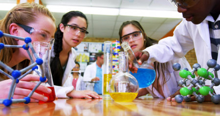 Pouring blue solution from beaker into flask in chemistry lab with lab coats and goggles. Education, science, experimentation, laboratory, collaboration, discovery, researchの写真素材