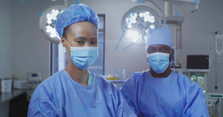 Standing surgeons wearing scrubs preparing for surgery in operating room, overhead lights. Medical,...
