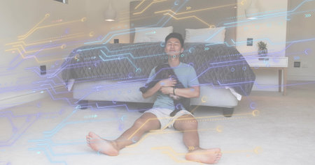 Cradling small dog, adult Asian man leaning by bed on bedroom floor, with digital circuit overlay. Futuristic, comfort, relaxation, technology, serenity, modern, companionshipの写真素材