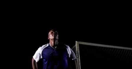 Gazing soccer player wearing jersey under stadium lights at night on field, with goalpost and net. Athlete, stadium, nighttime, athletic, competition, sport, focusの写真素材