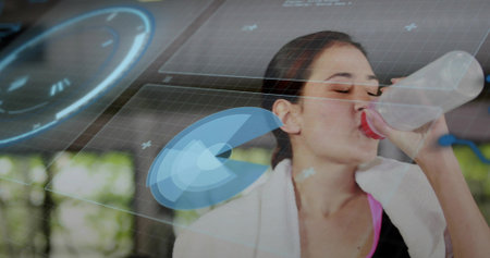 Pausing woman in sports top drinking from water bottle in studio with towel window bars holograms....