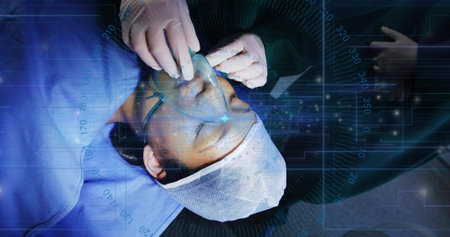 Gloved clinician placing anesthesia mask over patient in OR, with digital monitoring overlays....