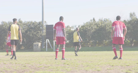 Holding soccer ball, Hispanic player wearing yellow bib standing on grassy pitch, with scoreboard....
