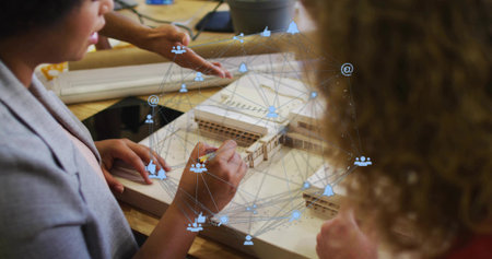Collaborating designers wearing blazers sketching wooden scale model in studio, with overlay icons....