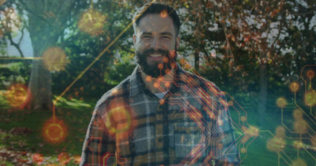 Smiling bearded man in flannel shirt standing in garden with autumn leaves, glowing circuit overlay....