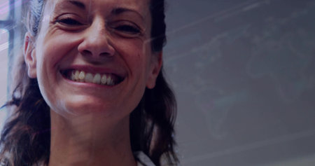 Smiling mid adult woman wearing white collared shirt in workspace, showing data on glass board....