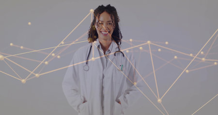 Standing female doctor wearing lab coat and stethoscope in studio, showing golden network nodes. Medical, healthcare, technology, innovation, professionalism, digital, diagnosticの写真素材
