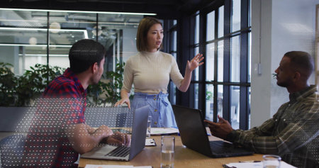 Presenting woman in beige top, blue skirt leading meeting at conference room, with open laptops....