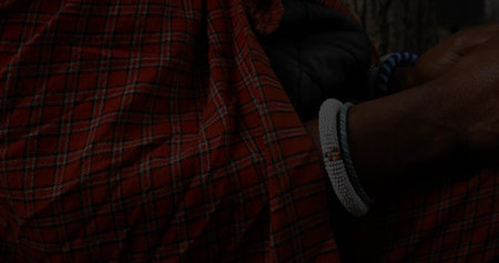 Posing man wearing red checkered wrap and white-blue beaded bracelets beside forest tree trunk. Heritage, tradition, rustic, natural, spirituality, cultural, outdoorの写真素材