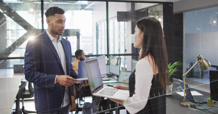Collaborating colleagues reviewing printed documents and sharing laptop in open plan office. Professional, teamwork, modern, corporate, productivity, workspace, collaborationの写真素材