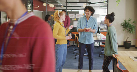 Chatting three coworkers holding coffee cups and mugs at modern open-plan office, with sticky notes....